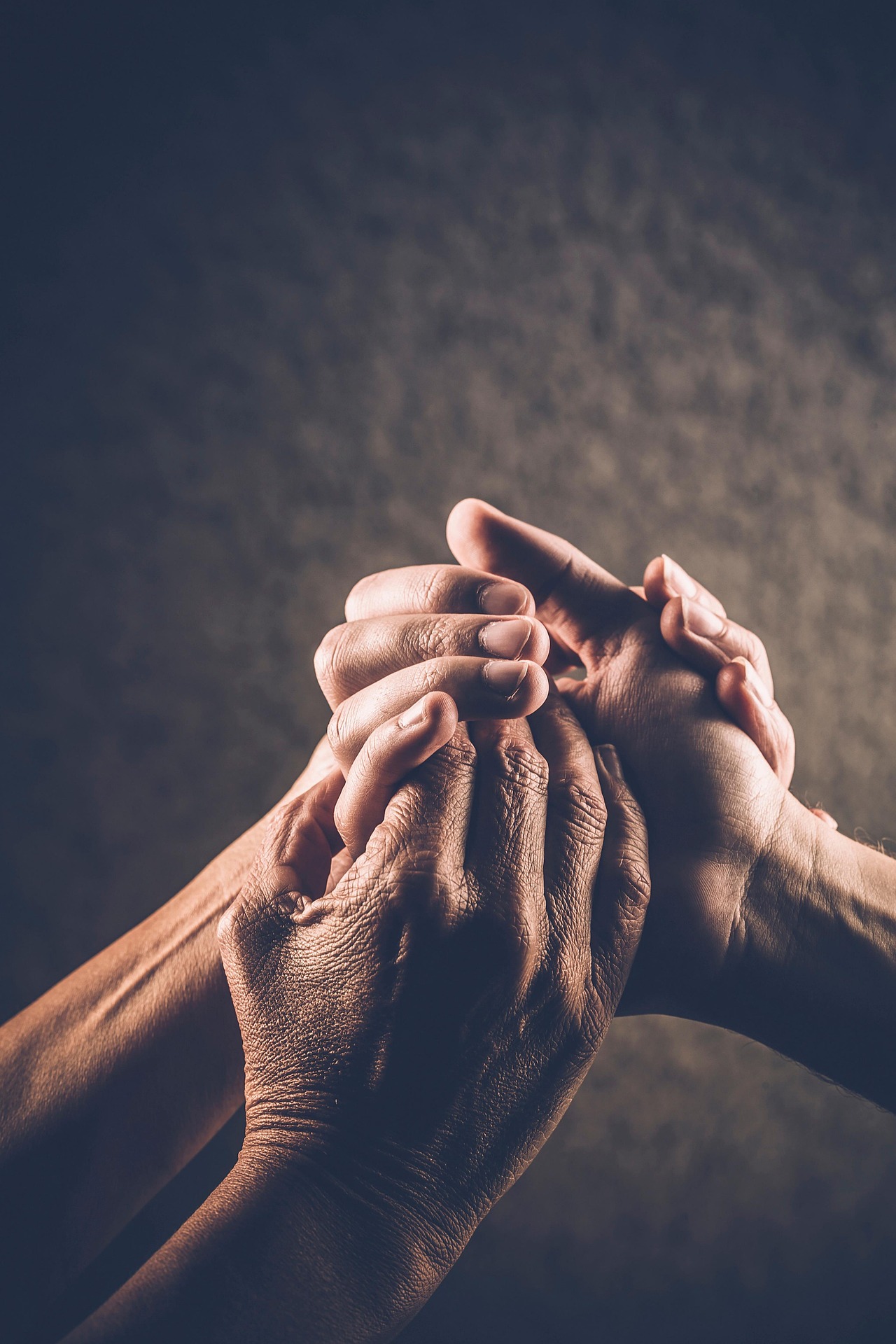 Foto de três mãos unidas de pessoas de diferentes idades. 