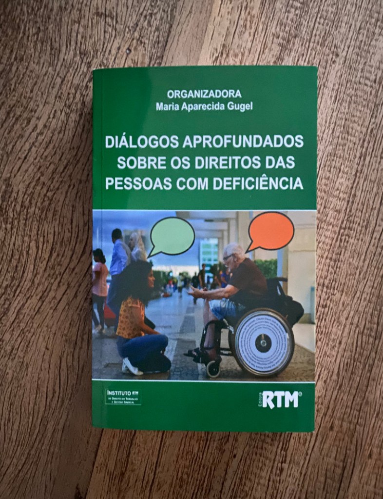 Foto com livro sobre uma mesa de madeira. Livro com capa em verde com o título Diálogos aprofundados sobre os direitos das pessoas com deficiência". Abaixo o título uma foto de duas pessoas conversando uma delas em uma cadeira de rodas. Abaixo a imagem o nome RTM da editora do livro.